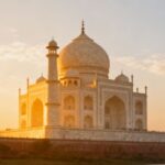 Taj Mahal glowing softly in silver-white marble under a clear full moon and starry night sky, viewed from a distance with peaceful surroundings.