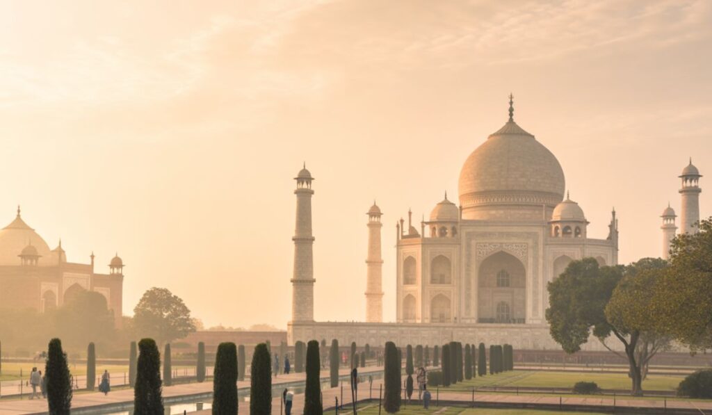 The Taj Mahal at sunrise with gardens and reflection pool in front.