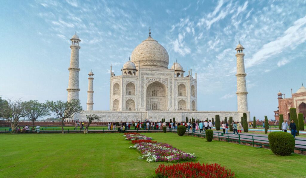 Tourists exploring the iconic Taj Mahal during a same day Agra tour, with lush green gardens and clear blue sky in the background.