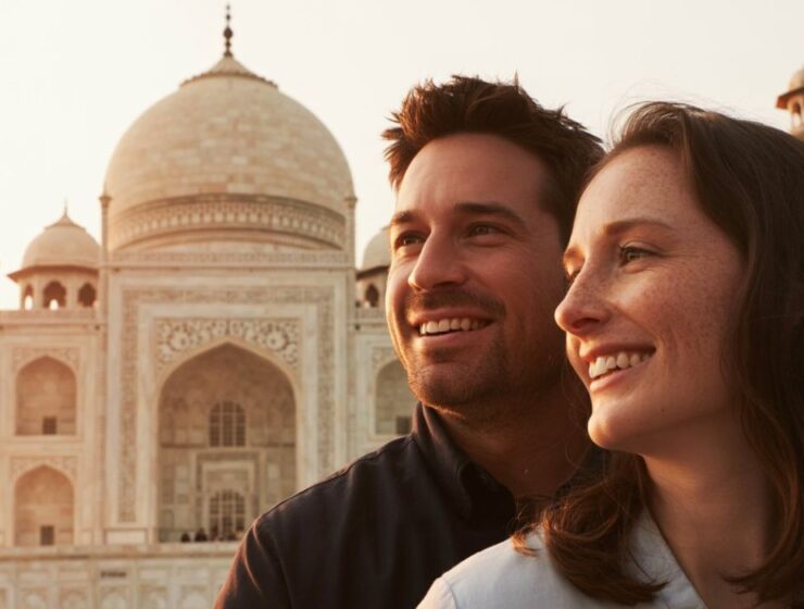 Smiling couple enjoying a Delhi to Taj Mahal trip with the Taj Mahal in the background during sunrise.